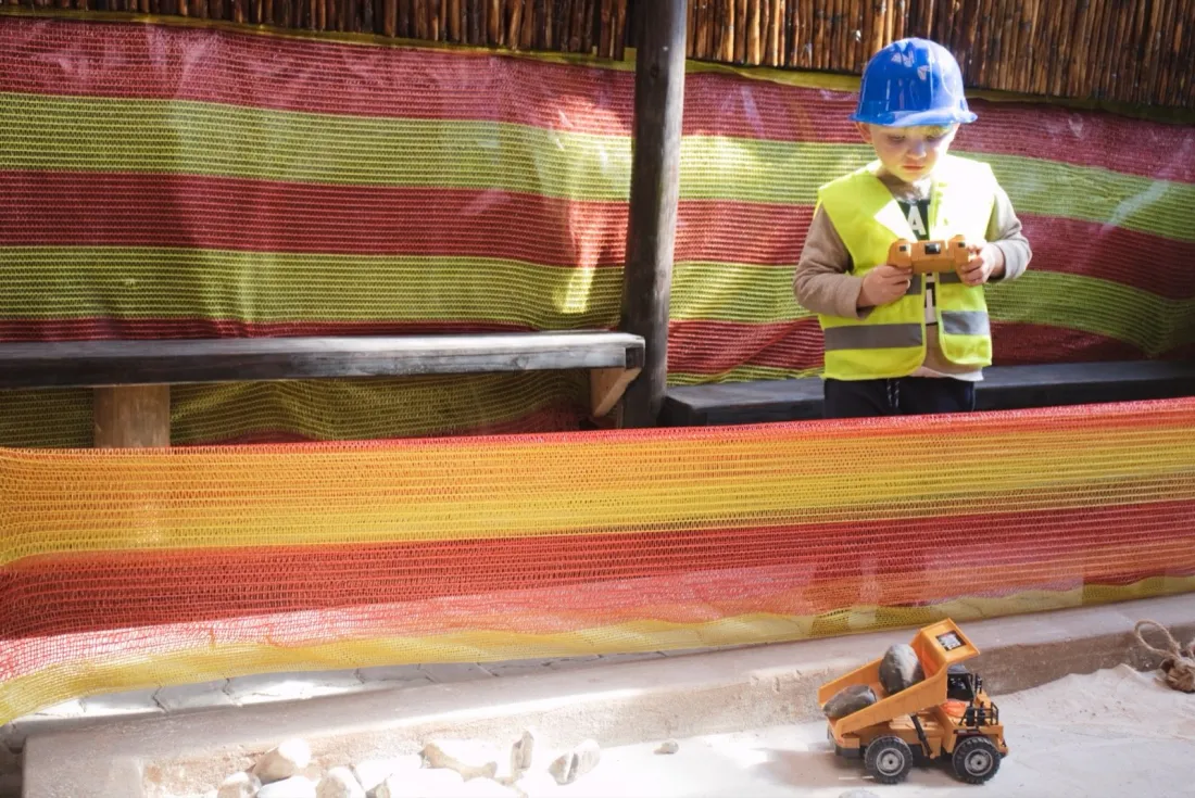 A child steering a remote-control dump truck along the sandy course under the shade netting